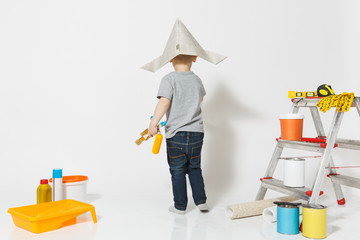 Little cute boy in newspaper hat with instruments for renovation apartment room isolated on white background. Wallpaper, gluing accessories, painting tools. Repair home. Parenthood, childhood concept.