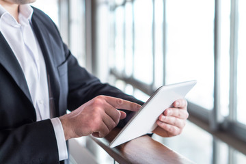 Business man using tablet by the window in modern glass office building. Businessman holding smart mobile device and working. Pressing touch screen with one finger. © terovesalainen