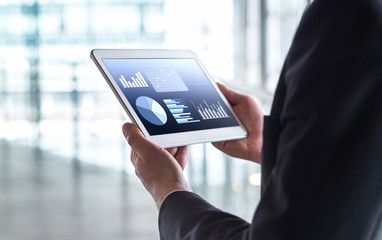 Man reading financial statistics, business graphs and trade data. Businessman using tablet in modern office building.