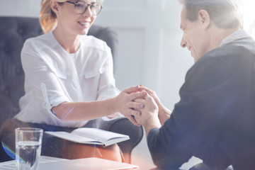 Obraz premium Professional therapist. Pleasant sympathetic female psychologist smiling and holding the hands of her patient while supporting hi,