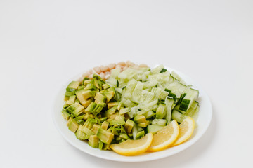 pieces of fresh avocados, cucumber slices, beans and lemon slices on plate on white background