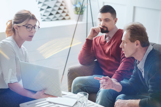 Team project. Nice pleasant male colleagues sitting of the sofa and talking about their project while looking at the laptop screen