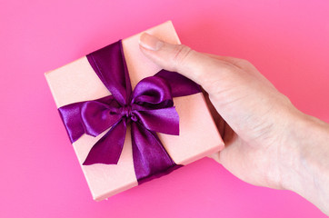 Hand keeps a present box on pink background