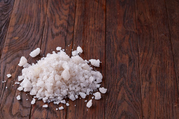 Pile of salt crystals on the dark wooden background, top view, flat lay, shallow depth of field