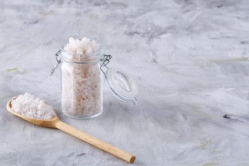 Spa concept. Bath salt pouring out of glass jar on texrured background, close-up, selective focus