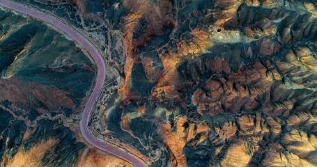 Aerial view on orange sandstone hills covered with sparse vegetation with curved, empty road...
