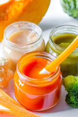 baby mashed with spoon in glass jar on white background