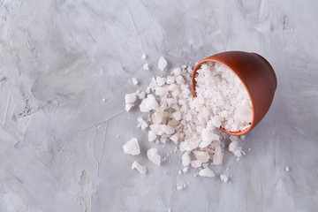 Composition of sea salt in ceramic bowl and spoon for cooking or spa on white background, top view, selective focus