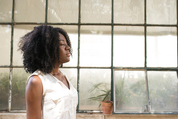 Calm black woman standing with closed eyes outdoors with greenhouse in background. Afro American...
