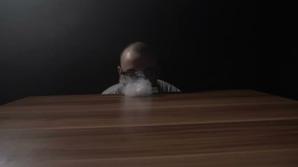 Young hipster teenager boy performing vaping tricks while making a steam wave on the table and then a tornado using his hand in slow motion