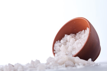 Composition of sea salt in ceramic bowl and spoon for cooking or spa on white background, top view, selective focus
