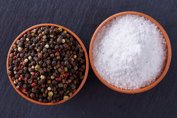 Conceptual composition of salt and pepper on spoons and bowls over light background, top view, close-up
