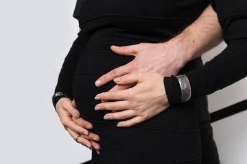 Hands of family members holding a belly of pregnant woman