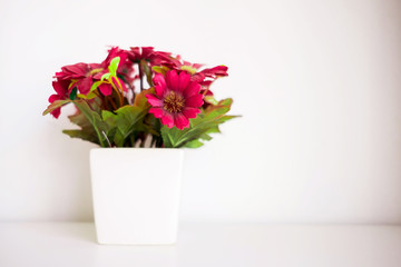 Still life fake red flowers in white pot on white table