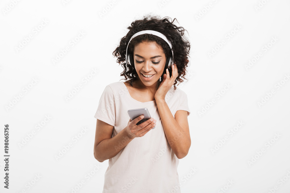 Wall mural young american woman with curly hairstyle listening to music and enjoying favourite song via wireles