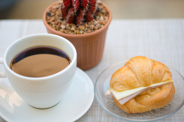 A cup of Black coffee with Ham and cheese croissant