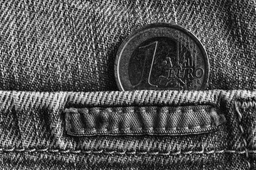 Euro coin with a denomination of 1 euro in the pocket of worn old denim jeans, monochrome shot