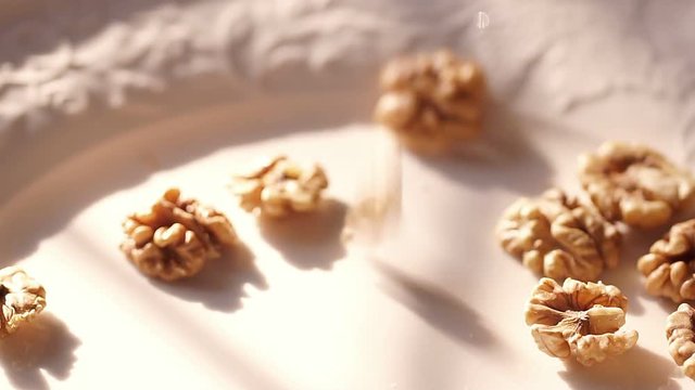 Walnut. Walnuts fall in slow-motion shot on a white plate. Slow-motion shot. Kitchen under the morning sun. A white plate with walnut