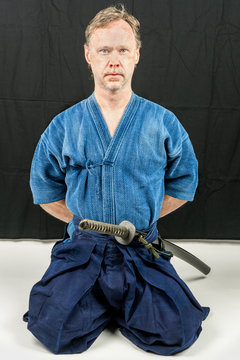 Caucasian male training Iaido, japanese sword sport. Hands behind his back. Sitting position.