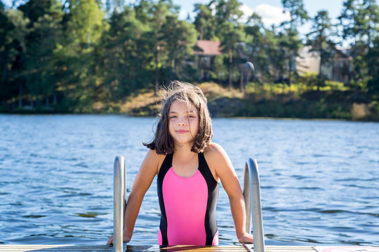 Cute little brown haired girl in swimsuit about to climb down in the water to swim.