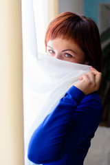 A beautiful woman in a blue dress is in the room near the window