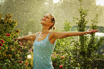 Portrait of a beautiful happy woman enjoying rain falling in her in a garden.