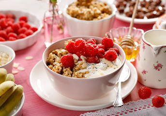 Granola with natural yogurt, raspberries, honey, almond flakes, and poppy seeds in a  bowl on a pink wooden table. A delicious and nutritious breakfast or dessert. Healthy eating concept