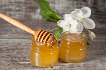 Honey dripping from a wooden honey dipper in a jar on wooden grey rustic background