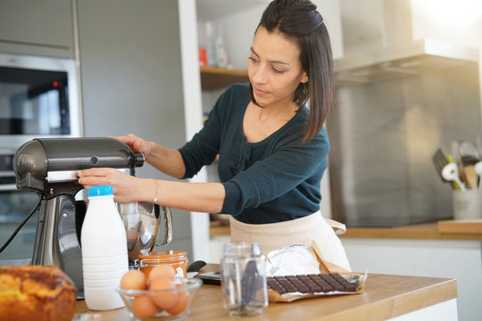Woman in kitchen preparing cake with pastry robot