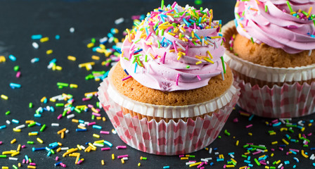 Closeup of cupcakes with vanilla, berries, pink and white cream, chocolate and sprinkles on wooden background. Selective focus. Sweet dessert tasty food concept muffin.