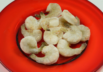 Frozen shrimp thawing out on red plate as part of meal cooking preparation