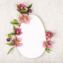 Creative layout with pink, red colorful flowers, leaves and egg shape on beige stone background. Easter concept, flat lay, top view and copy space.