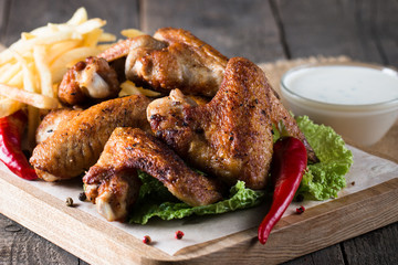 Close-up photo of bbq chicken wings with fries and beer. Barbeques meat with sauces, ketchup, mayonnaise. Fast and junk food concept. 