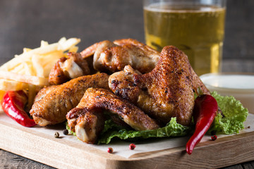 Close-up photo of bbq chicken wings with fries and beer. Barbeques meat with sauces, ketchup, mayonnaise. Fast and junk food concept. 