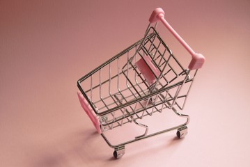 Shopping cart. Empty Supermarket trolley on pink background. Consumerism concept photo.
