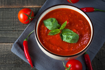 Chili tomato soup with sour cream sauce, cottage cheese, basil and red hot peppers on wooden background. Healthy, vegan and dieting lunch and dinner concept.