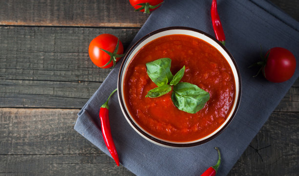 Chili tomato soup with sour cream sauce, cottage cheese, basil and red hot peppers on wooden background. Healthy, vegan and dieting lunch and dinner concept.