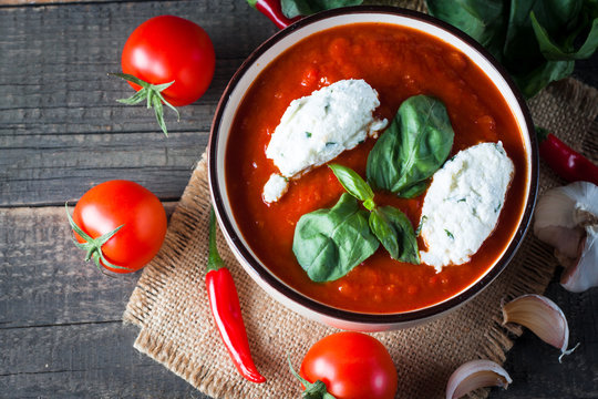 Chili tomato soup with sour cream sauce, cottage cheese, basil and red hot peppers on wooden background. Healthy, vegan and dieting lunch and dinner concept.