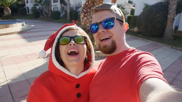 Happy couple in santa hats taking selfie picture from hands in summer outdoors
