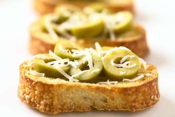 Crostini with green olive slices and freshly grated parmesan-like hard cheese, photographed with natural light (Selective Focus, Focus in the middle of the first crostini)