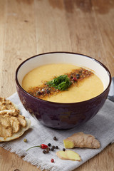 Ceramic bowl of pumpkin soup on napkin over rustic wooden background, close-up, selective focus, top view.