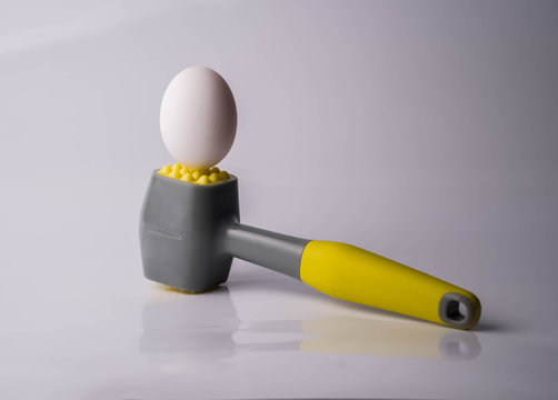 Egg and hammer on table. Symbol of strength, force and something hard and unbreakable. Concept of fragility and power.