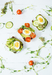 Tasty sandwiches with egg, avocado and vegetables on wooden white rustic background
