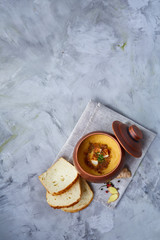 Clay pot of pumpkin soup on homespun napkin rustic wooden background, close-up, selective focus, top view.