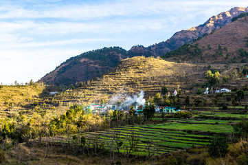 Landscape shot of Dehradun with a village on a hillside. The smoke coming from the village, the grassy stepped fields and beautiful surroundings make this a perfect tourism shot - Powered by Adobe