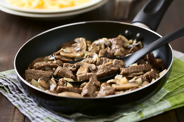 Beef Stroganoff in frying pan, a dish made of pieces of beef, mushroom and onion in cream sauce, photographed with natural light (Selective Focus, Focus in the middle of the dish on the spoon)
