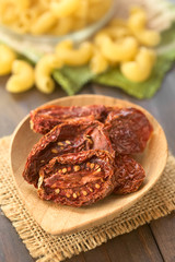Sun-dried tomato halves on bamboo plate with raw pasta in the back, photographed with natural light (Selective Focus, Focus in the middle of the first tomato half)
