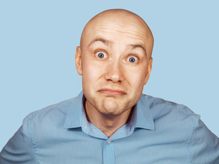 Close up portrait of frightened young bald guy. Isolated on blue background.