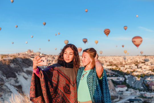 traveler enjoying valley view and making selfie on a phone with wonderful balloons flight over Cappadocia valley in Turkey