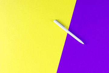 Top view of white ballpoint pen on yellow and violet background